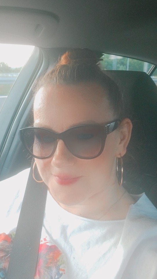 Kobieta w okularach przeciwsłonecznych, siedząca w samochodzie z zapiętym pasem, sugerująca podróż z firmą transportową.