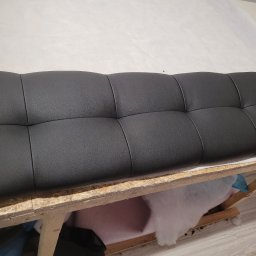 BMT TAPICER Patryk Kowalczuk - Czarny, pikowany panel tapicerowany na drewnianym stelażu, widoczne wypełnienie z waty. Detal z warsztatu tapicerskiego, bliski kadr.