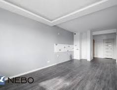 Jasne wnętrze po remoncie: szare ściany, ciemna podłoga imitująca drewno, biały sufit z podświetleniem. Fragment dekoracyjnej mozaiki na ścianie. Minimalistyczny styl.