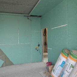 SVEET PRO - Wnętrze w trakcie wykańczania: ściany pokryte płytami gipsowo-kartonowymi, widoczne przewody elektryczne, narzędzia i materiały izolacyjne Knauf. Surowy betonowy sufit.