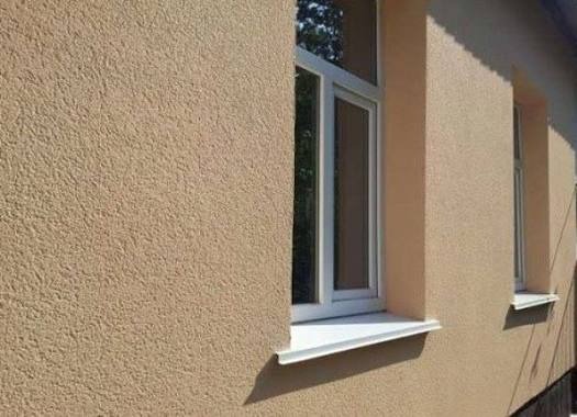 Elewacja budynku z oknami po nałożeniu tynku strukturalnego w odcieniach beżu. Widoczne detale faktury tynku i białe ramy okienne.