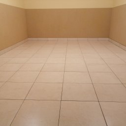 MI-TA group Sp.z.o.o. - Beżowe płytki podłogowe ułożone w kwadraty, ściany w odcieniach beżu i kremu. Pusta przestrzeń po remoncie, gotowa do umeblowania. Neutralne kolory.