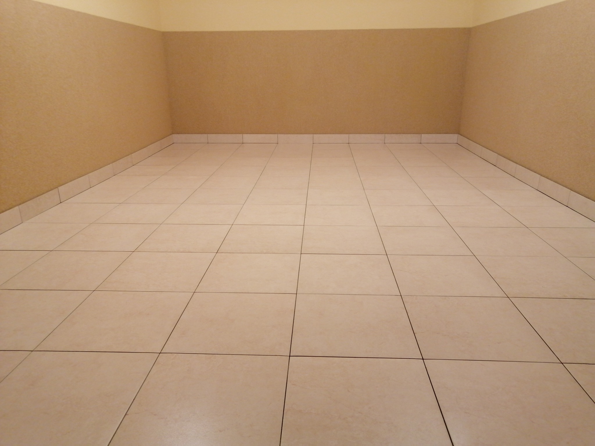 Beżowe płytki podłogowe ułożone w kwadraty, ściany w odcieniach beżu i kremu. Pusta przestrzeń po remoncie, gotowa do umeblowania. Neutralne kolory.