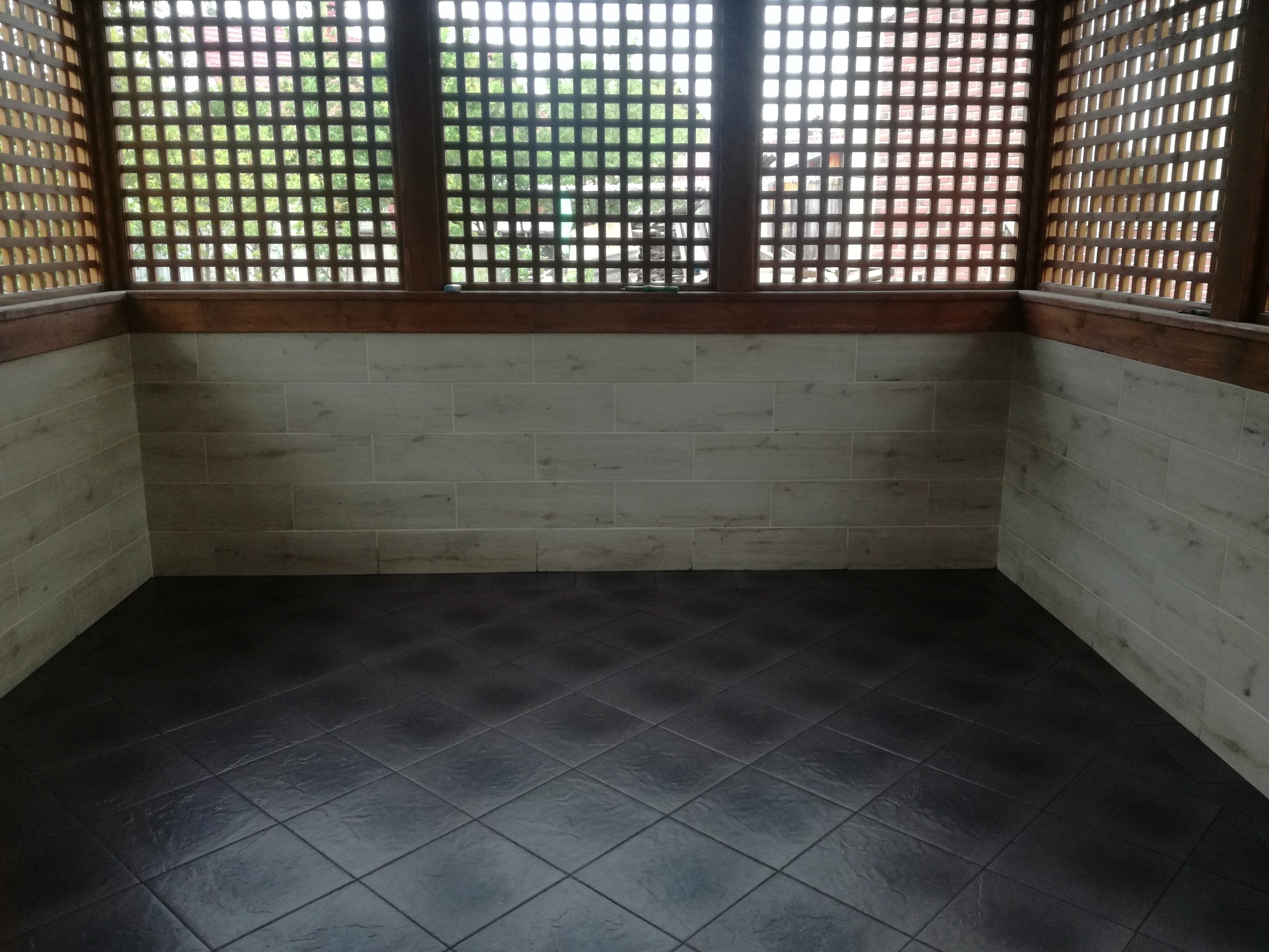 Wykończony balkon z brązową kratką, beżowymi płytkami ściennymi i ciemną podłogą z płytek. Widok na zewnątrz przez kratkę.