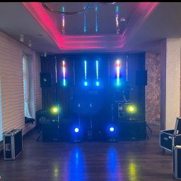 Mateusz Zabiegły - Sala z nagłośnieniem i oświetleniem gotowa na imprezę. Widoczne kolumny, reflektory i skrzynie transportowe. Na suficie dekoracyjne oświetlenie LED.