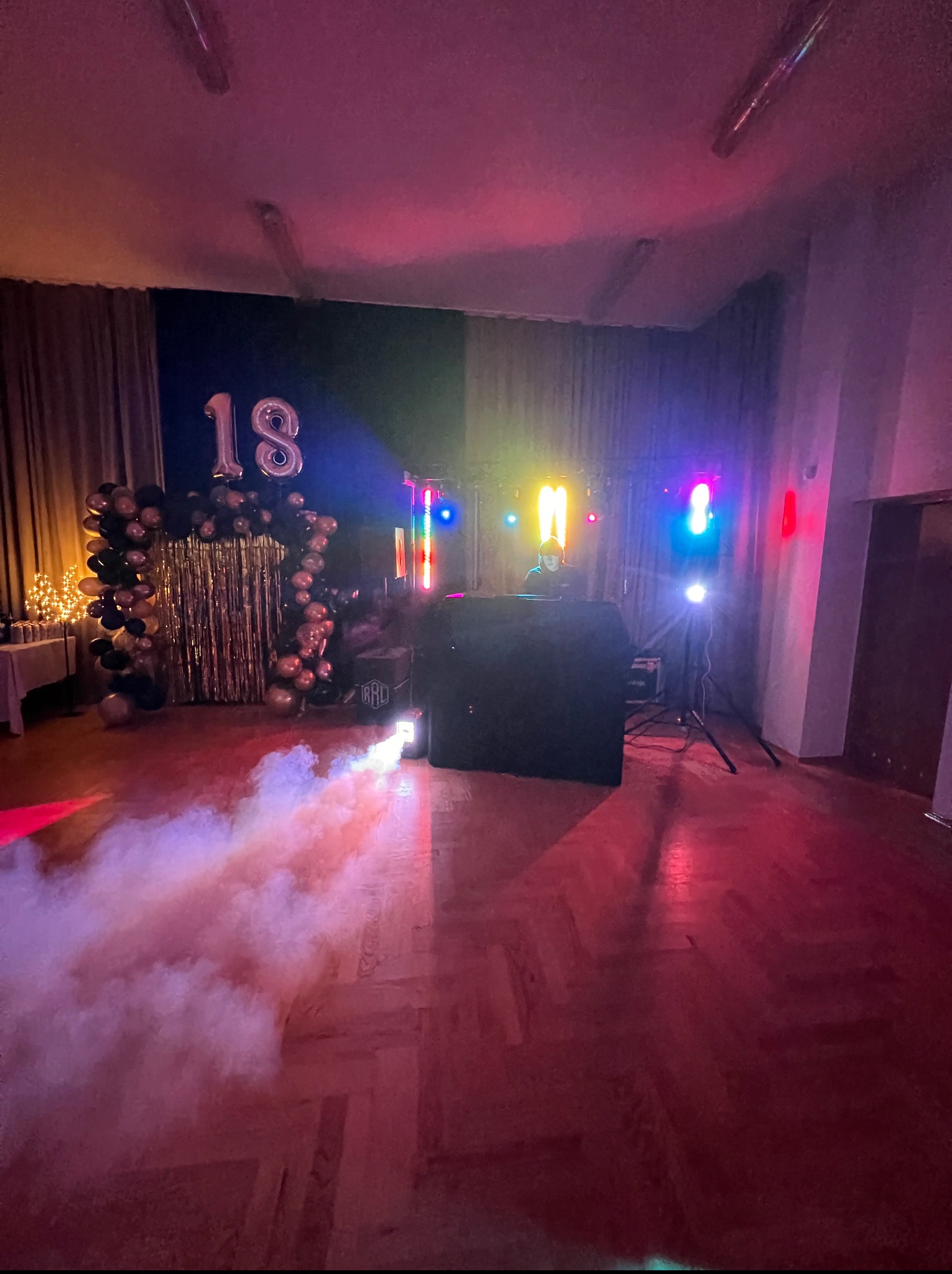 Uroczystość 18-nastkowe z dekoracją balonową, DJ-em i oświetleniem scenicznym, z efektem dymu na parkiecie w sali.