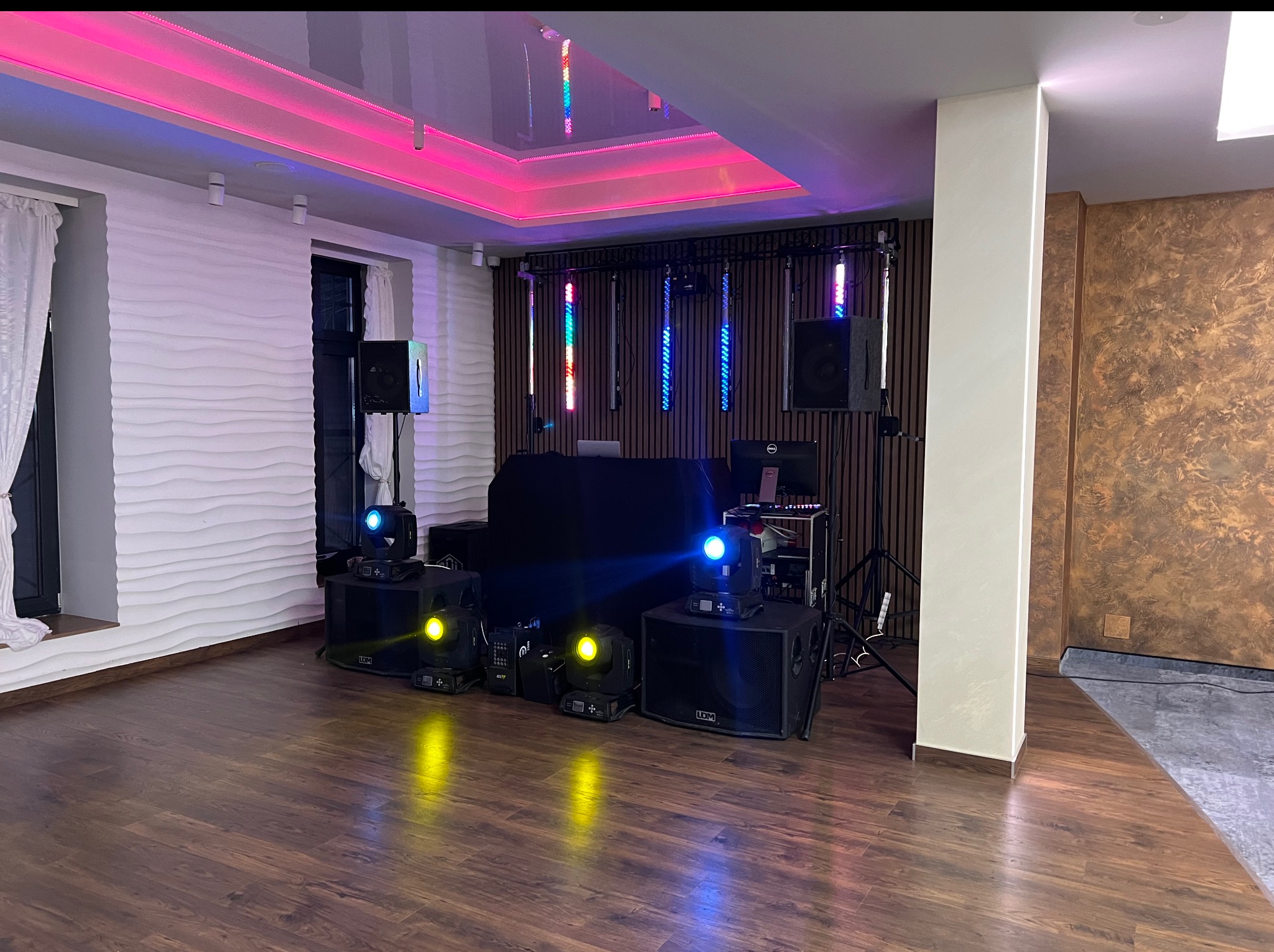 Sala z parkietem, przygotowana na imprezę. Widoczne nagłośnienie, oświetlenie sceniczne, reflektory i dekoracje świetlne na suficie. Gotowość do wydarzenia.