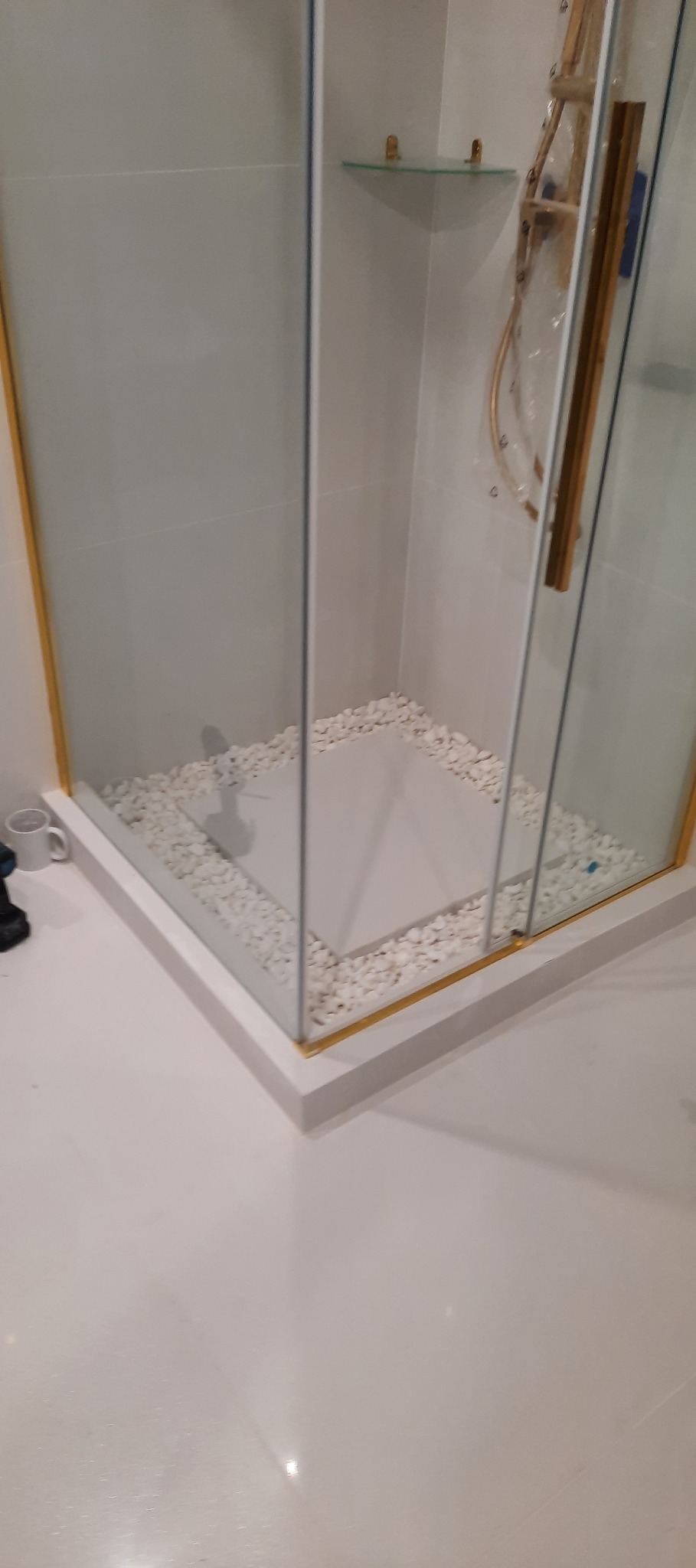 Nowoczesna kabina prysznicowa z białymi kamykami dekoracyjnymi i złotymi akcentami, widok z góry. Minimalistyczny design w jasnej łazience.