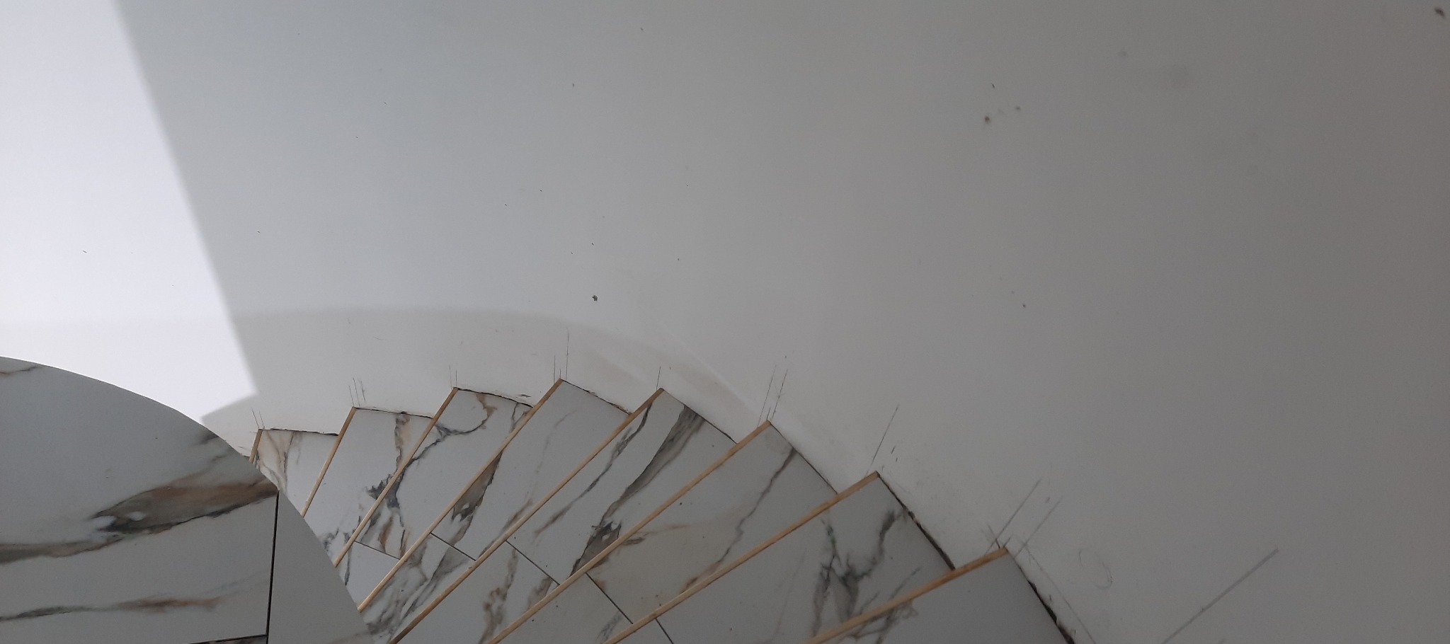 Wykończone płytkami schody z wzorem marmuru, widoczne od góry, z białymi ścianami w tle. Detale wykończenia i precyzja ułożenia płytek.