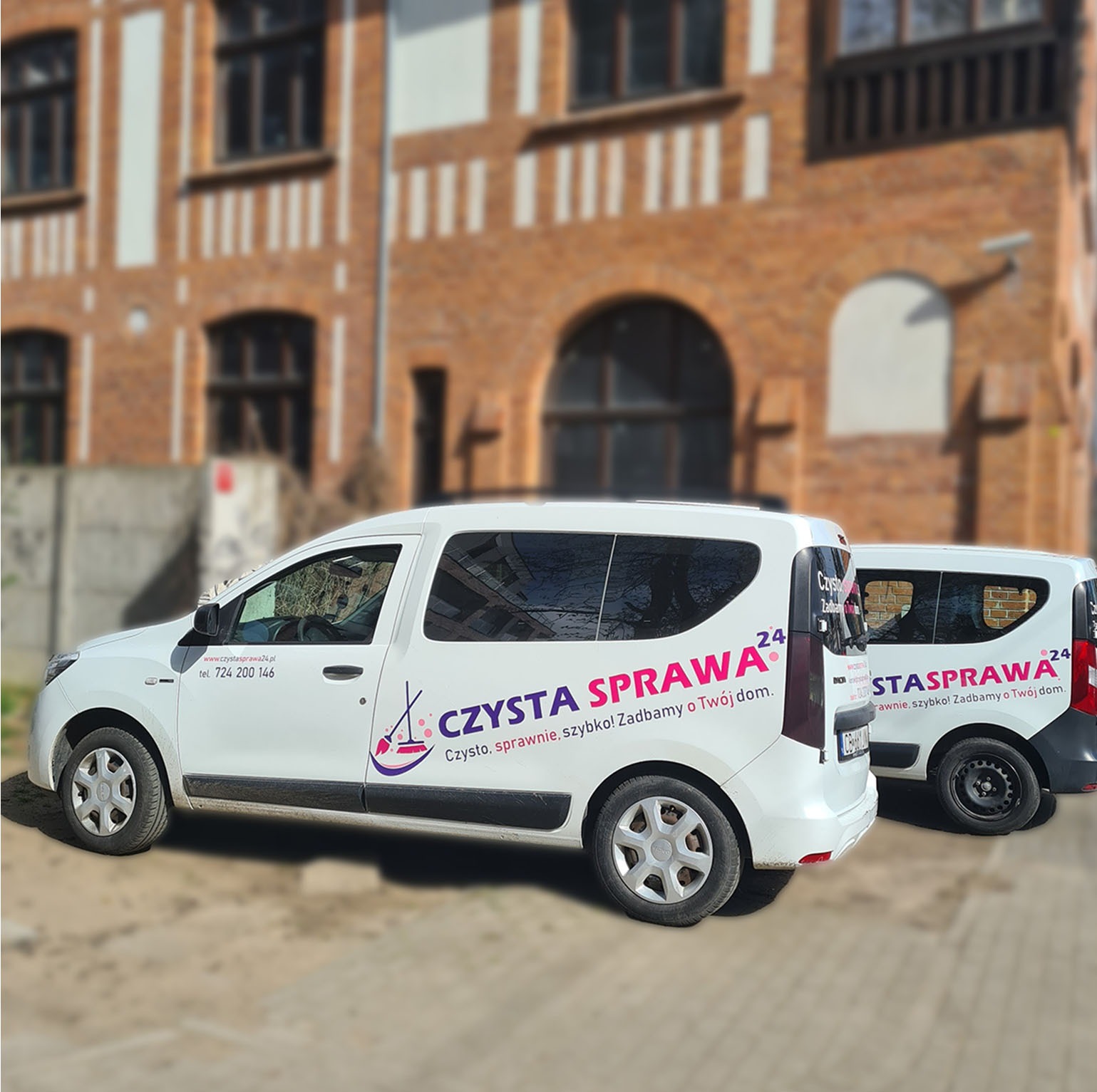 Dwa białe samochody firmy sprzątającej 'Czysta Sprawa 24' z logo i numerem telefonu na tle ceglanego budynku. Jeden z pojazdów jest lekko rozmazany.