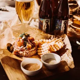 Apetyczna kompozycja: burger z warzywami, frytki waflowe, sosy i piwo kraftowe na drewnianej desce, w ciepłym oświetleniu. Gastronomiczna fotografia.