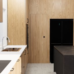 KIKU STUDIO Małgorzata Kudlik - Nowoczesna kuchnia z drewnianymi frontami, białym blatem i wyspą z ciemnego marmuru. W tle czarna lodówka i ukryte drzwi. Minimalistyczny design, jasne wnętrze.