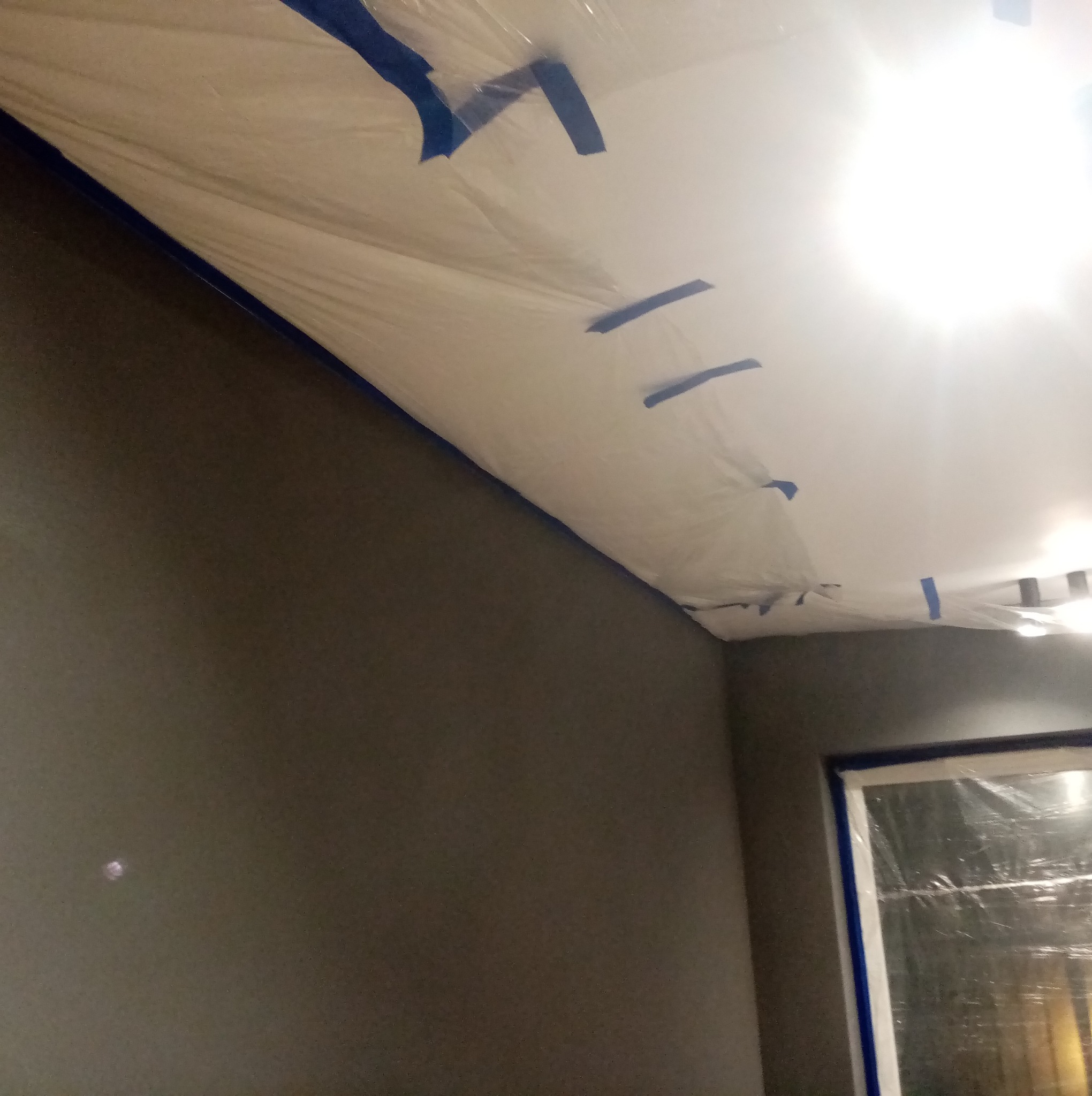 Przygotowanie do malowania: ściana w kolorze grafitowym, sufit zabezpieczony folią malarską i niebieską taśmą. Okno również zabezpieczone folią.