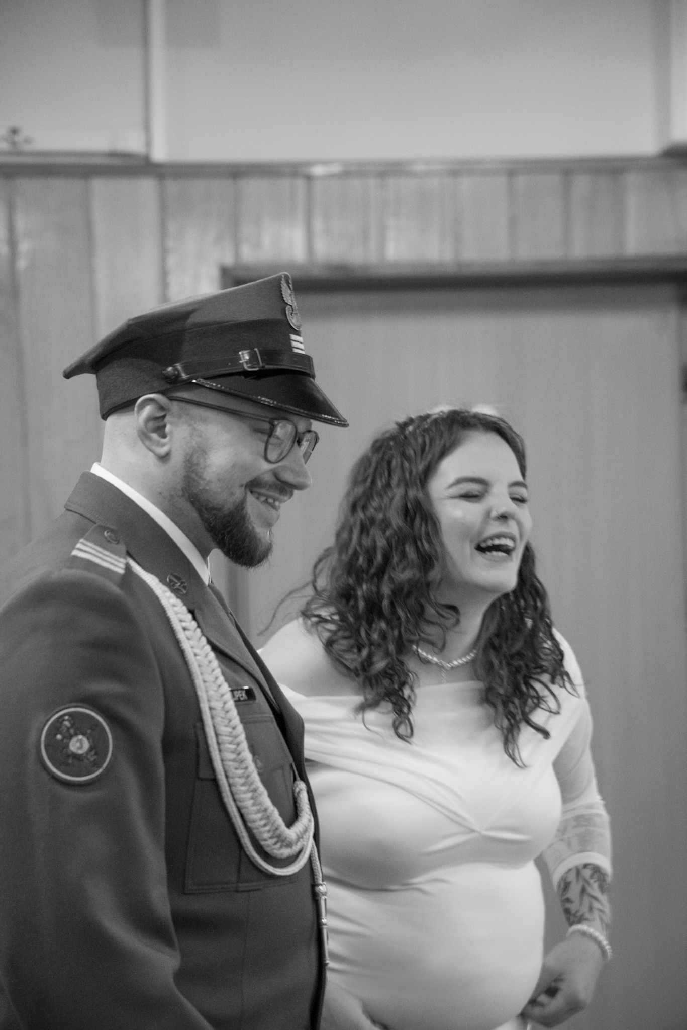 Czarno-białe zdjęcie uśmiechniętej pary: mężczyzna w mundurze oficerskim i kobieta w białej sukience. Ujęcie z profilu, z widocznymi detalami munduru i fryzury kobiety.