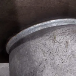 Spoina łącząca rurę z blachą, widoczna z bliska, szara powierzchnia metalu zarysowana, spaw wykonany precyzyjnie.