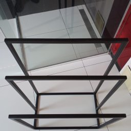 Marek Paruzel - Czarna, metalowa konstrukcja regału z trzema półkami na tle białych i czarnych płytek w łazience. Widoczne mocne spawy na rogach.