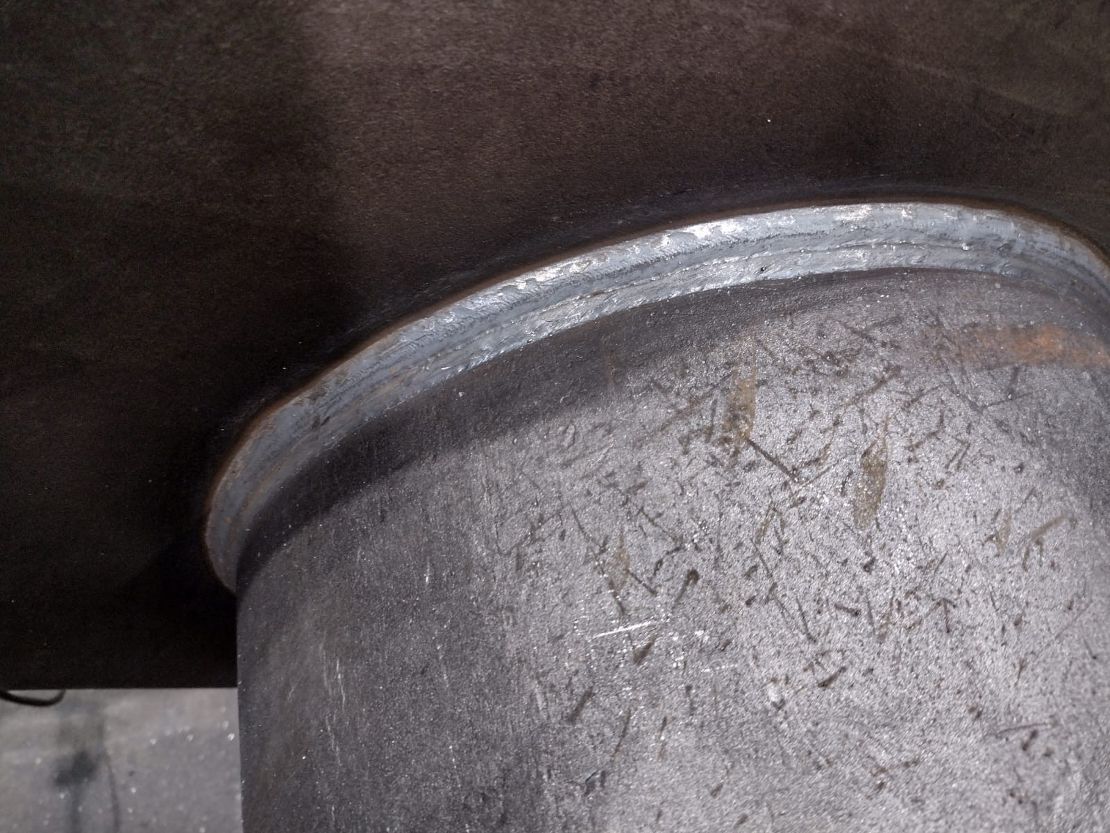 Spoina łącząca rurę z blachą, widoczna z bliska, szara powierzchnia metalu zarysowana, spaw wykonany precyzyjnie.