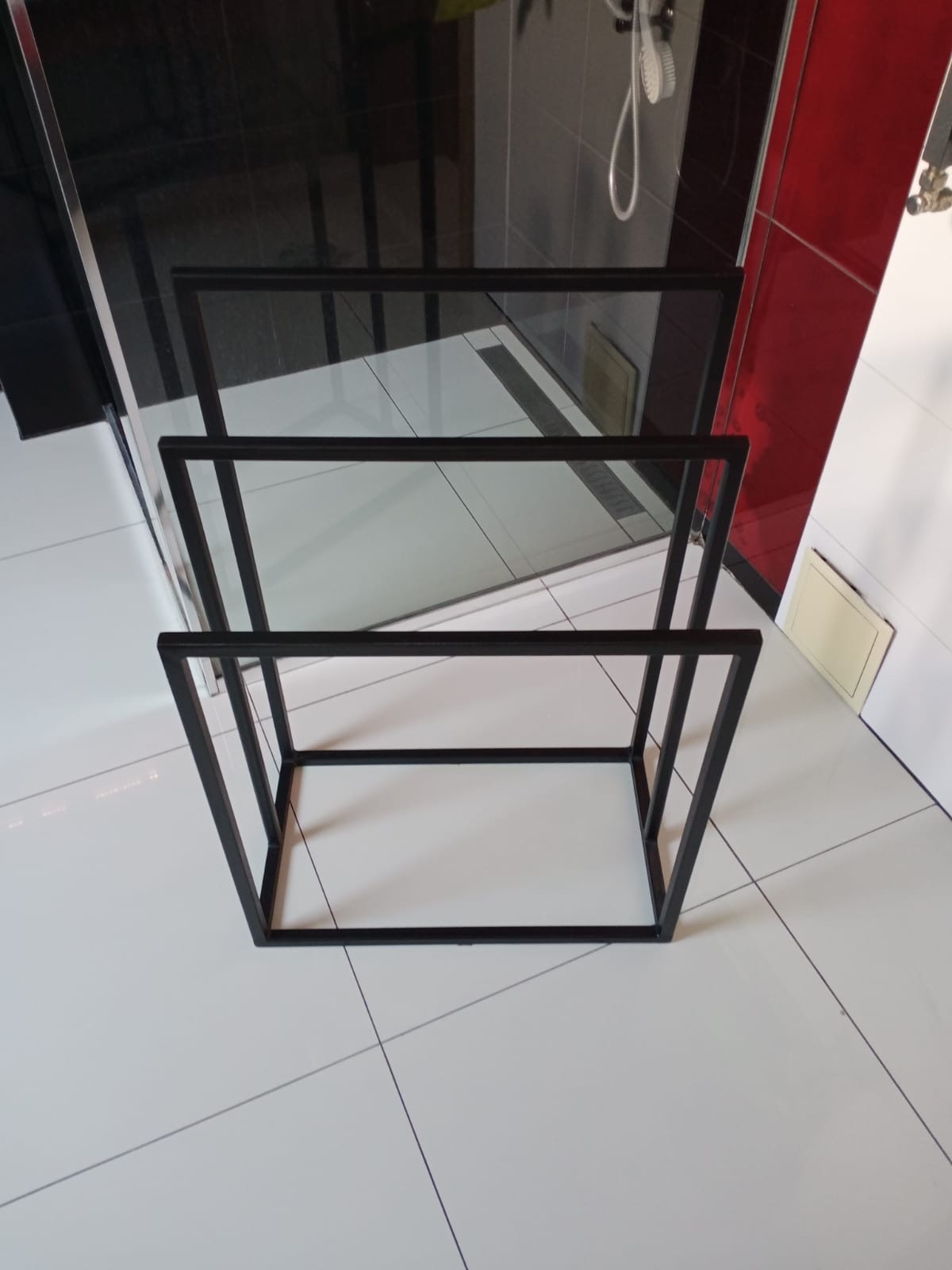 Czarny, metalowy stojak na ręczniki w nowoczesnej łazience z białymi i czerwonymi płytkami, widok z góry, minimalistyczny design.