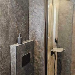 Remonty Pod Klucz - Nowoczesna łazienka z kabiną prysznicową typu walk-in, grafitowymi płytkami imitującymi kamień i czarną armaturą. Minimalistyczny design, spójna kolorystyka.
