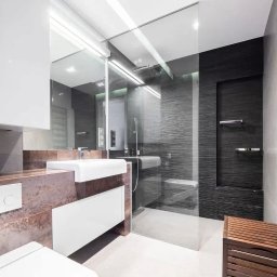 Remonty Pod Klucz - Nowoczesna łazienka z kabiną prysznicową typu walk-in, umywalką na blacie z elementami miedzi i grzejnikiem drabinkowym. Minimalistyczny design, eleganckie wykończenie.
