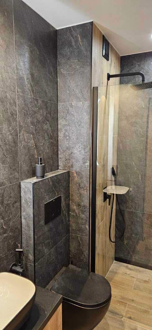 Nowoczesna łazienka z kabiną prysznicową typu walk-in, grafitowymi płytkami imitującymi kamień i czarną armaturą. Minimalistyczny design, spójna kolorystyka.