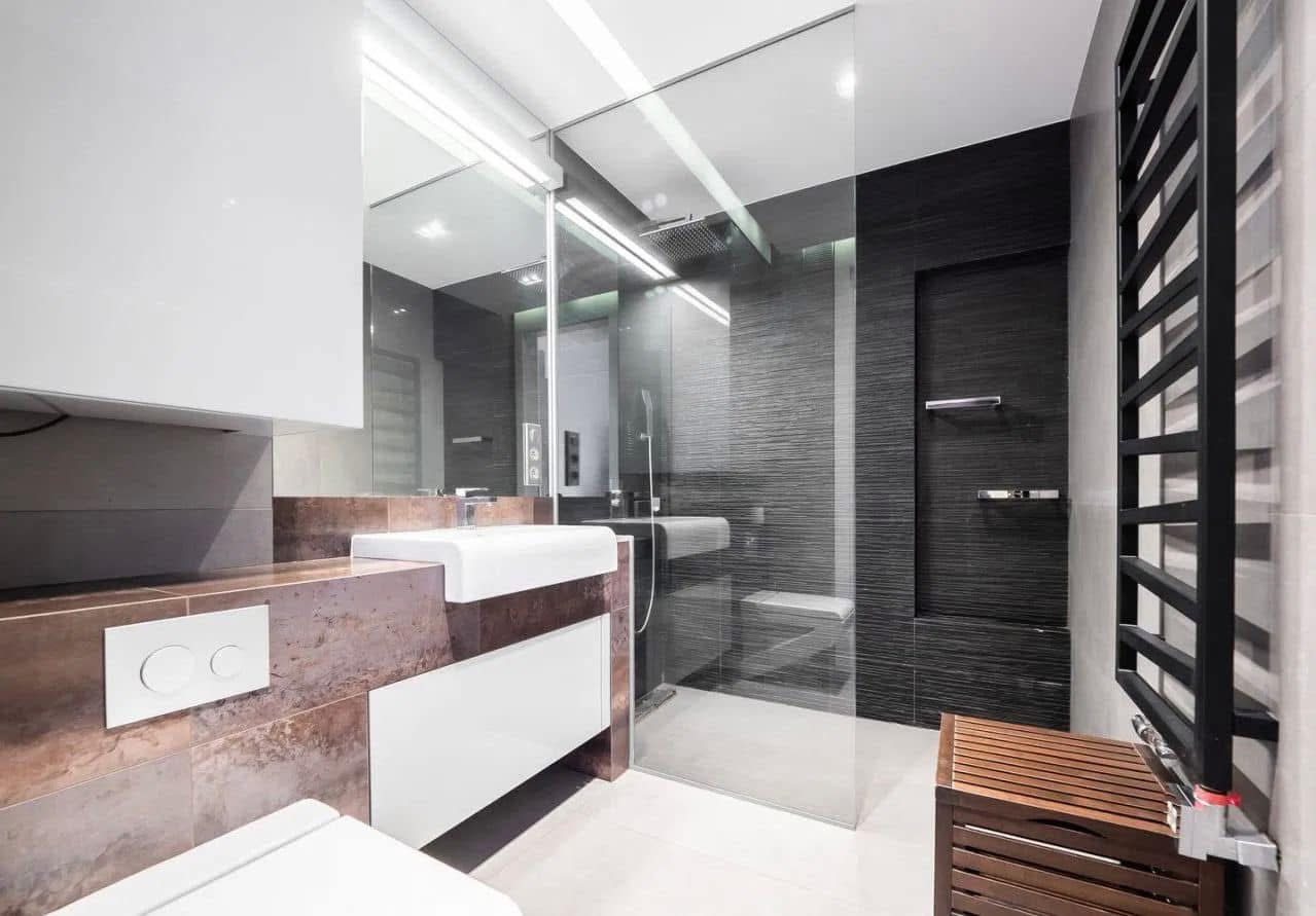 Nowoczesna łazienka z kabiną prysznicową typu walk-in, umywalką na blacie z elementami miedzi i grzejnikiem drabinkowym. Minimalistyczny design, eleganckie wykończenie.
