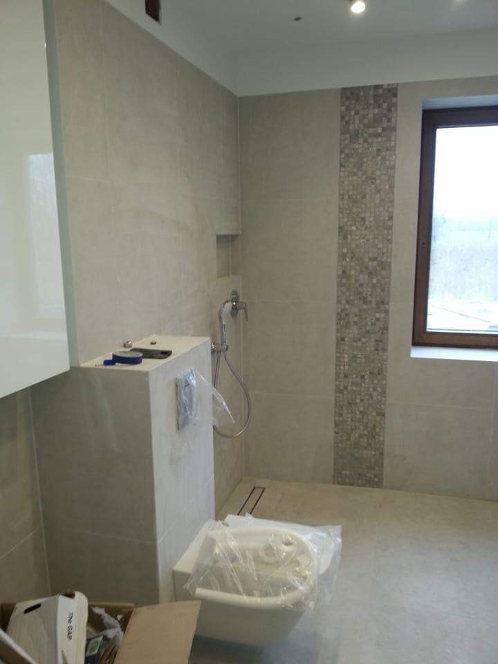 Jasna łazienka w trakcie wykańczania: beżowe płytki, mozaika dekoracyjna, zabudowa WC, bidet w folii ochronnej, okno z widokiem na zewnątrz. Minimalistyczny design.