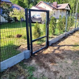 P.H.U HURTOWNIA STALI JUSTYNA KOBUS - Nowoczesne ogrodzenie panelowe z furtką, osadzone na betonowej podmurówce, w tle dom z panelami solarnymi i zielony ogród. Słoneczny dzień.