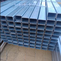 P.H.U HURTOWNIA STALI JUSTYNA KOBUS - Stalowe, prostokątne profile ogrodzeniowe ułożone w stos. Elementy zabezpieczone plastikowymi taśmami. Widoczny fragment kostki brukowej w tle.