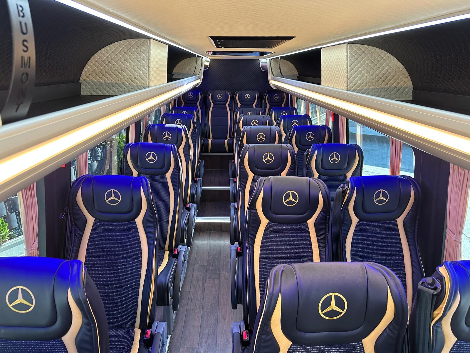 Wnętrze luksusowego busa Mercedes z niebiesko-złotymi fotelami. Widok na rzędy siedzeń, oświetlenie LED i schowki bagażowe. Elegancki design i komfort podróży.