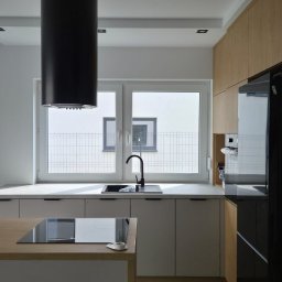 IVAN ANDRUSYSHYN - Nowoczesna kuchnia z wyspą i czarnym okapem cylindrycznym. Jasne szafki, biały blat, okno z widokiem na ogrodzenie. Minimalistyczny design.