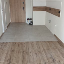 IVAN ANDRUSYSHYN - Połączenie paneli podłogowych i płytek w nowym mieszkaniu. Widoczne fragmenty instalacji elektrycznej i wodnej. Świeżo wykończone wnętrze w jasnych kolorach.