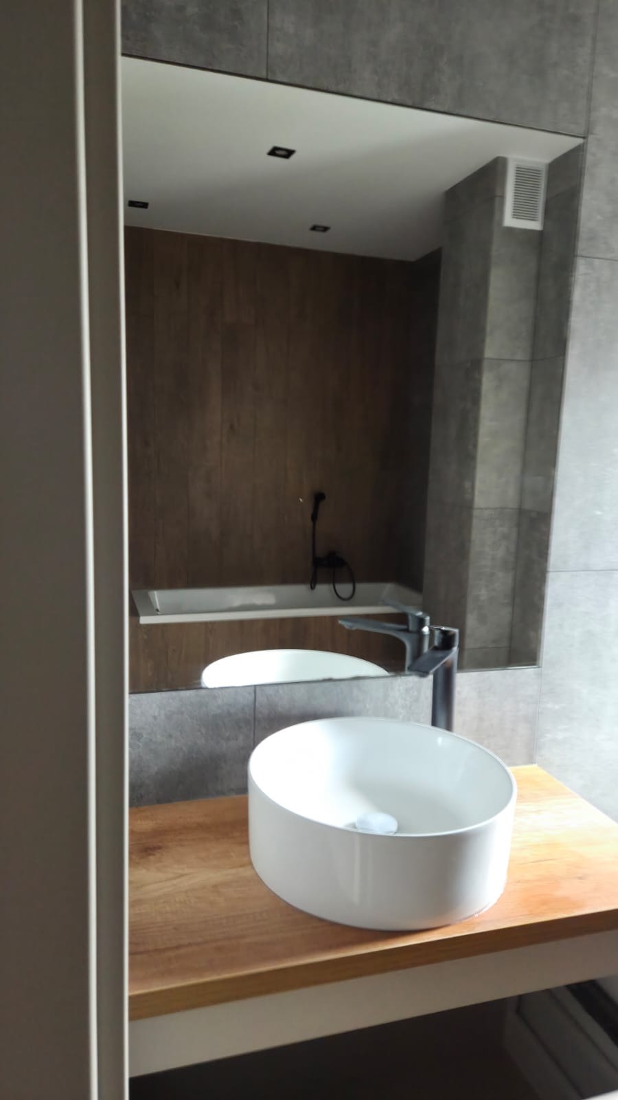 Nowoczesna łazienka w Ciasnej: biała umywalka nablatowa na drewnianym blacie, szara płytka, minimalistyczna armatura i oświetlenie punktowe, odbicie w lustrze.