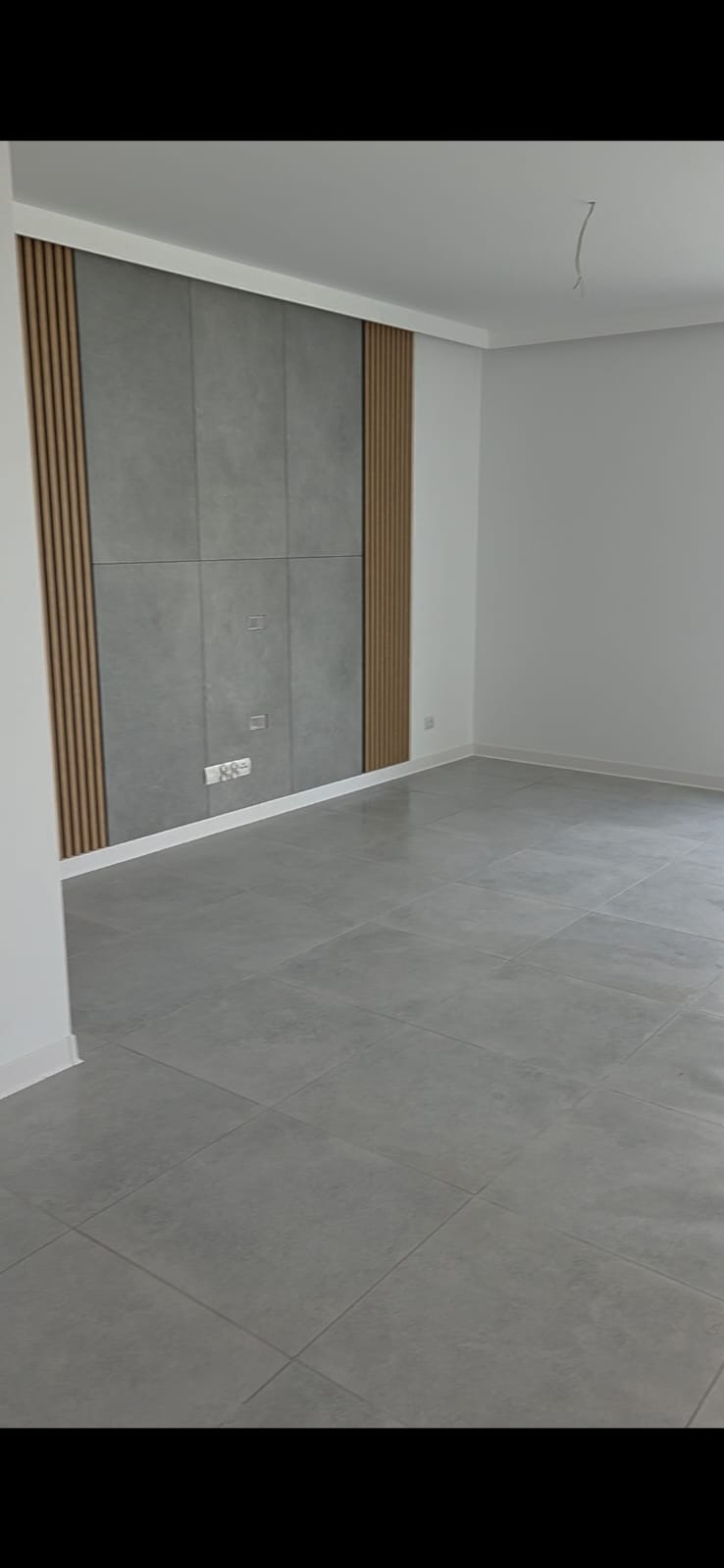 Szare płytki podłogowe i dekoracyjna ściana z panelami w odcieniach szarości i drewna, w nowocześnie wykończonym, pustym pokoju.