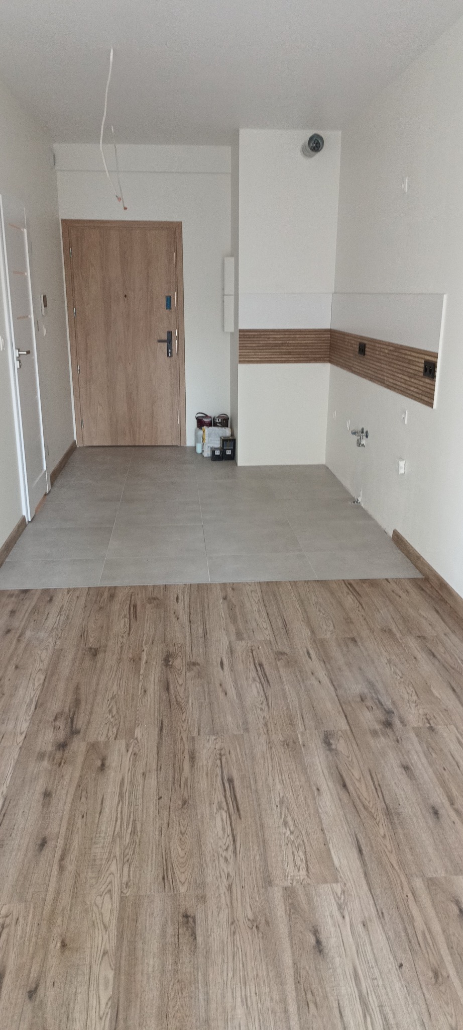 Połączenie paneli podłogowych i płytek w nowym mieszkaniu. Widoczne fragmenty instalacji elektrycznej i wodnej. Świeżo wykończone wnętrze w jasnych kolorach.