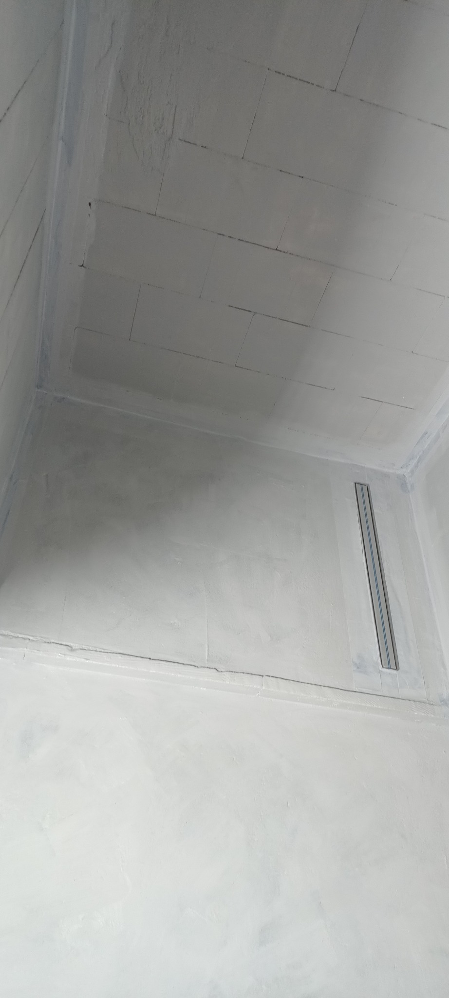 Wnętrze kabiny prysznicowej z odpływem liniowym, przygotowanej do położenia płytek. Widoczne ściany i sufit po szpachlowaniu, z zaznaczonym układem płytek.