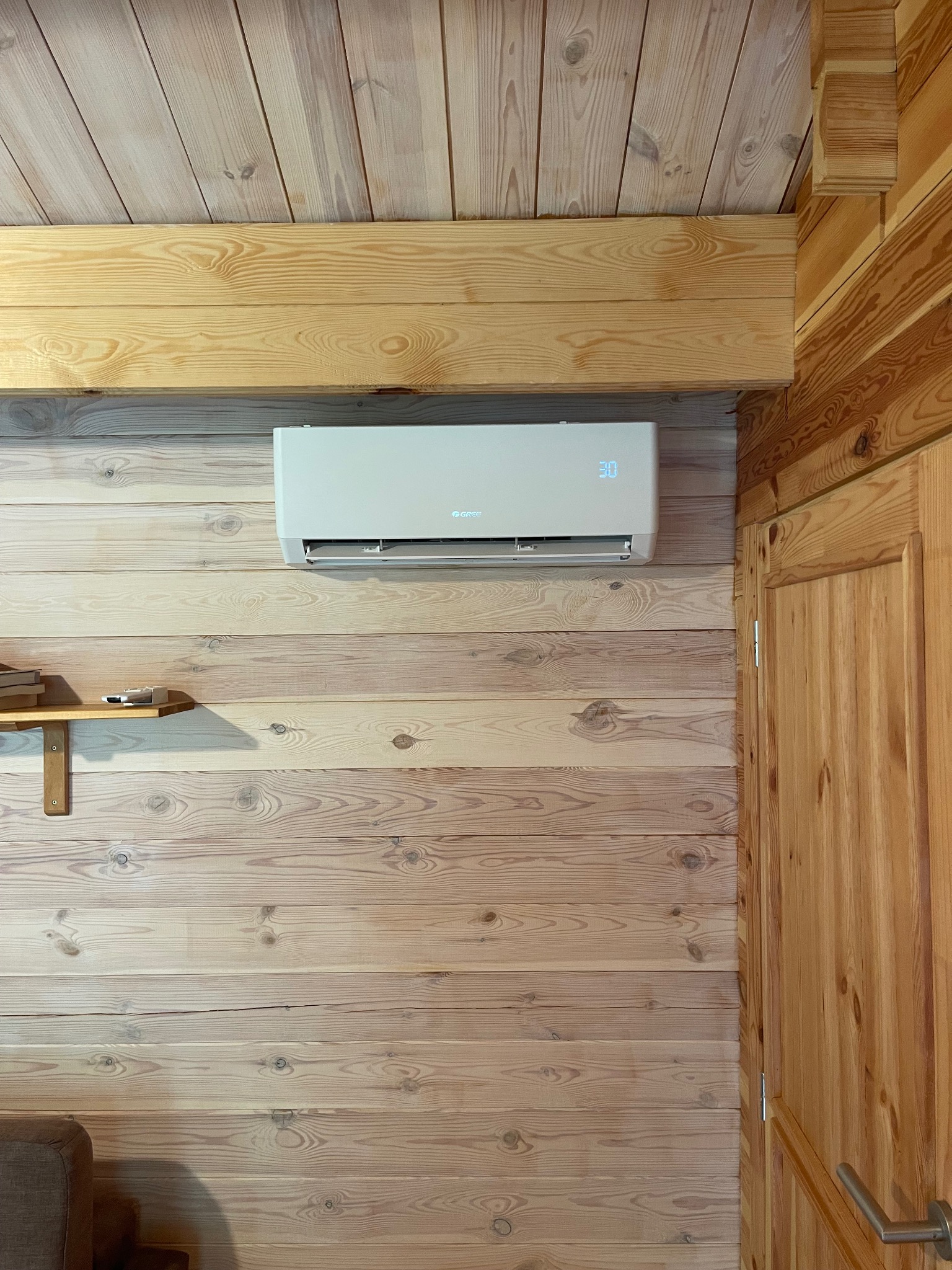 Klimatyzator ścienny marki Gree, ustawiony na 30 stopni, zamontowany w drewnianym wnętrzu z boazerią i elementami wykończeniowymi z jasnego drewna.