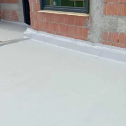 Wykończony dach płaski z obróbkami blacharskimi przy ścianie z pustaków ceramicznych i oknem. Widoczna membrana dachowa w jasnym kolorze.