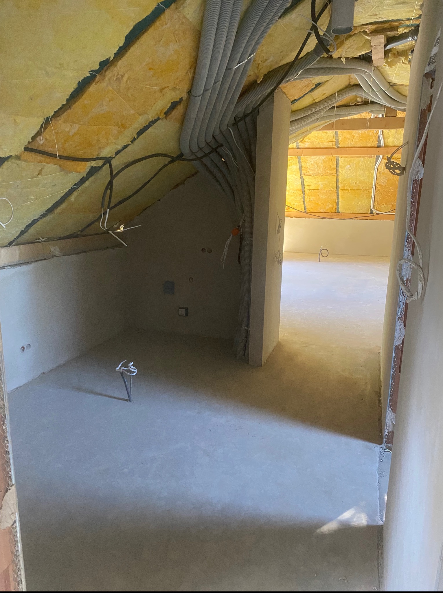 Poddasze z ociepleniem, instalacją elektryczną w peszlach i świeżo wylaną posadzką. Widoczne ściany po szpachlowaniu. Stan surowy zamknięty, przygotowany do dalszych prac wykończeniowych.