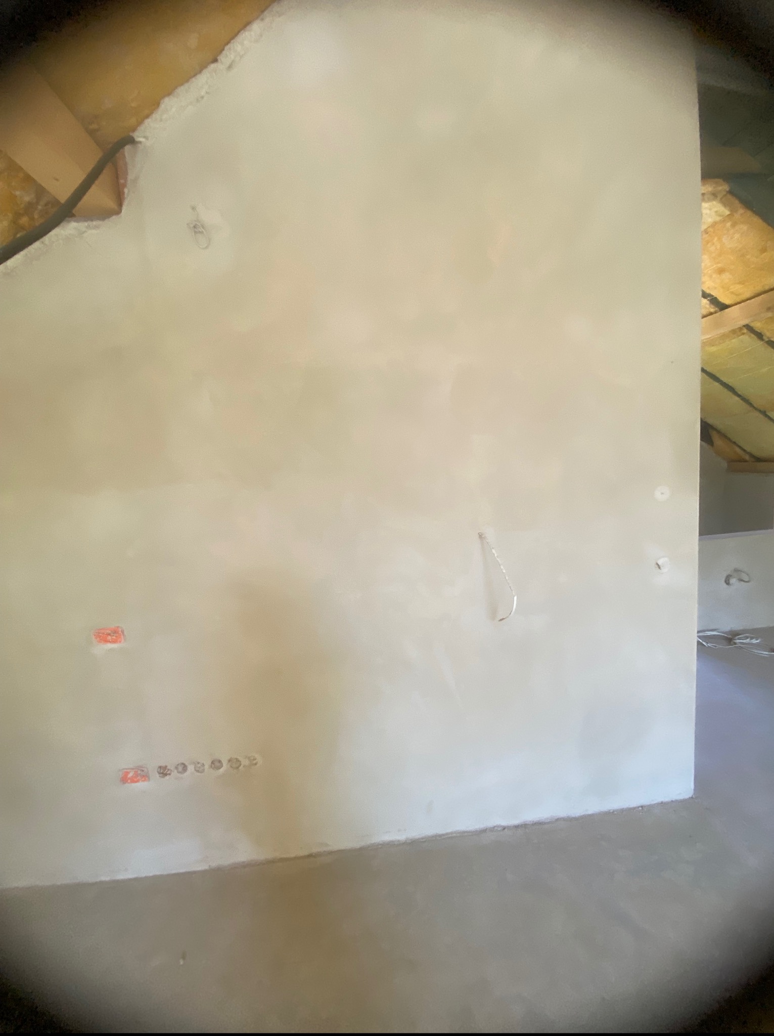 Ściana po nałożeniu gładzi, widoczne punkty elektryczne i fragment poddasza. Świeżo wykończona powierzchnia gotowa do dalszych prac wykończeniowych.