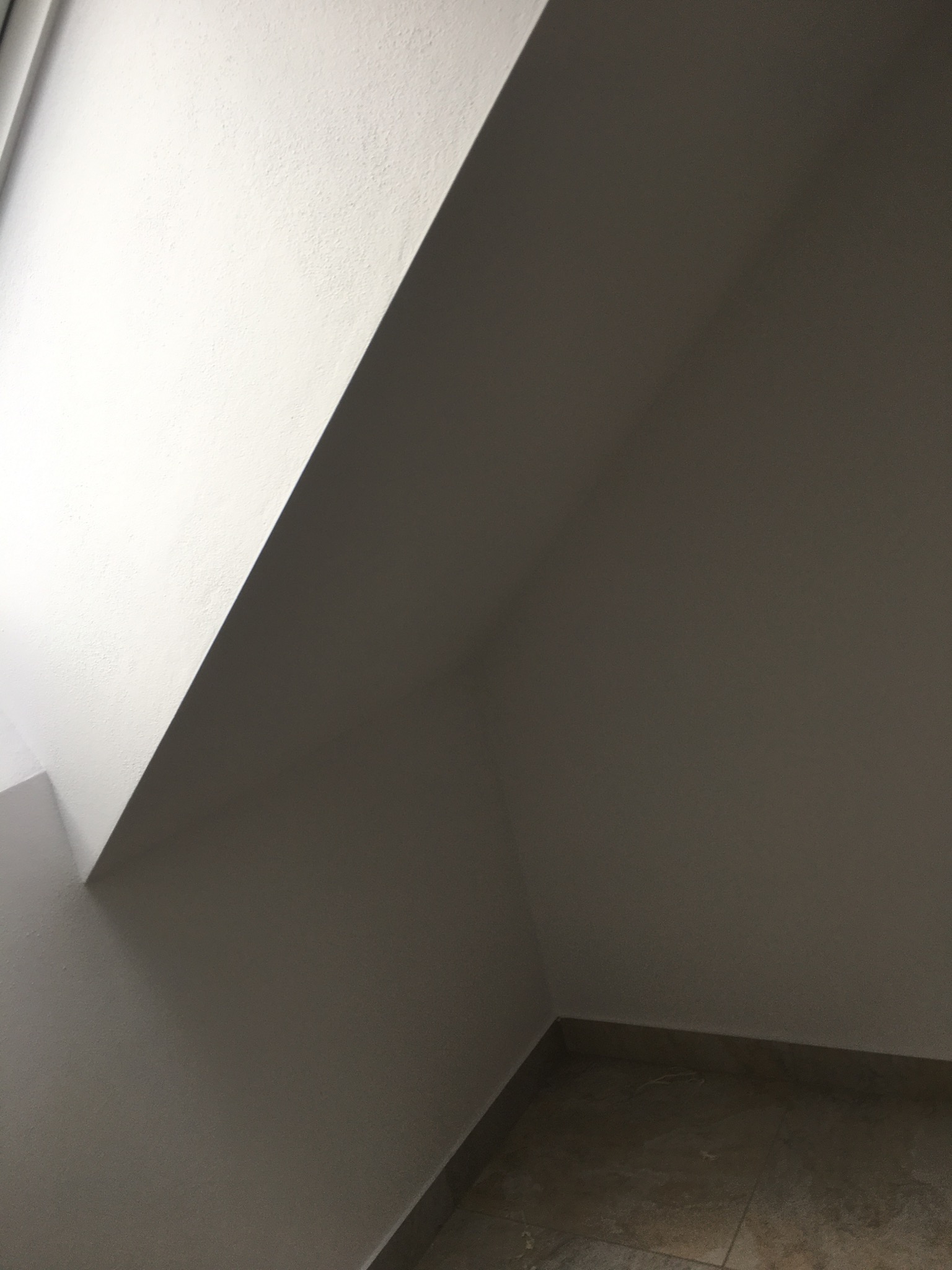 Ściana po szpachlowaniu i malowaniu na biało, widoczny fragment podłogi z płytek. Ujęcie z dołu, podkreślające gładką powierzchnię ściany i kąt padania światła.