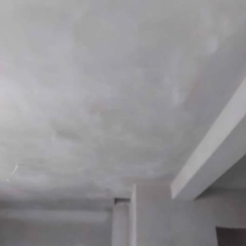 Surowy, jasnoszary sufit po nałożeniu tynku, widoczny fragment ściany i filar. Powierzchnia nierówna, przygotowana do dalszych prac wykończeniowych.