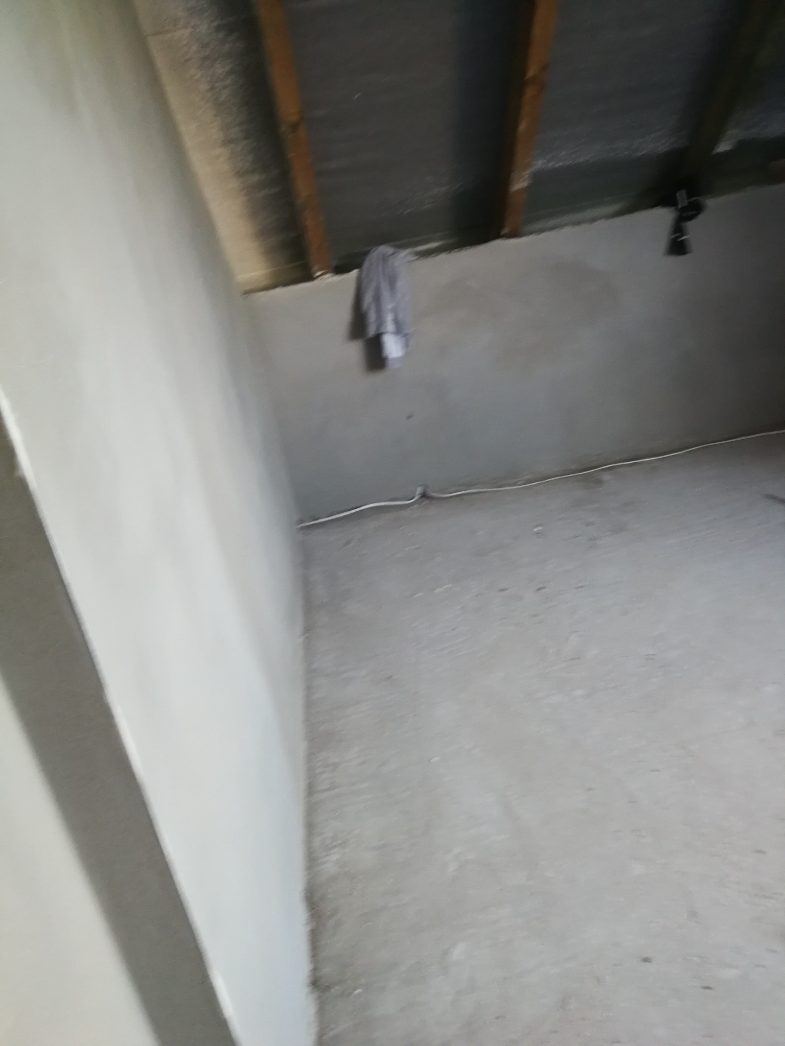 Wnętrze poddasza po nałożeniu gładzi, widoczne ściany i podłoga w szarym odcieniu, surowe drewniane elementy konstrukcyjne dachu.