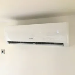 Biała klimatyzacja GREE zamontowana na jasnej ścianie, widoczne dwa włączniki. Na wyświetlaczu klimatyzacji widoczna temperatura 16 stopni.