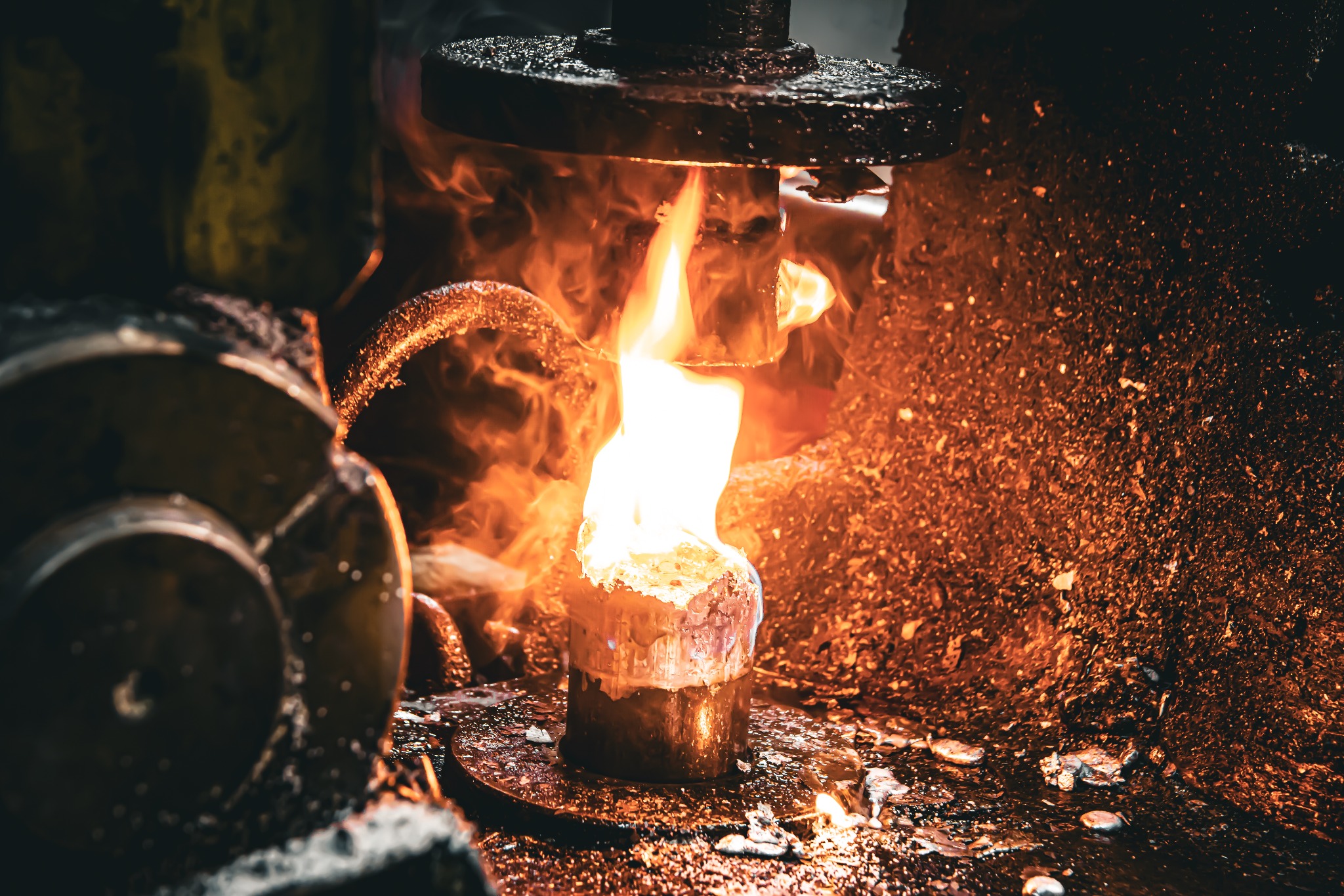 Rozgrzany metal pod naciskiem prasy, otoczony iskrami i płomieniami. Obróbka metalu w warsztacie, intensywne ciepło i dynamiczny proces kształtowania.