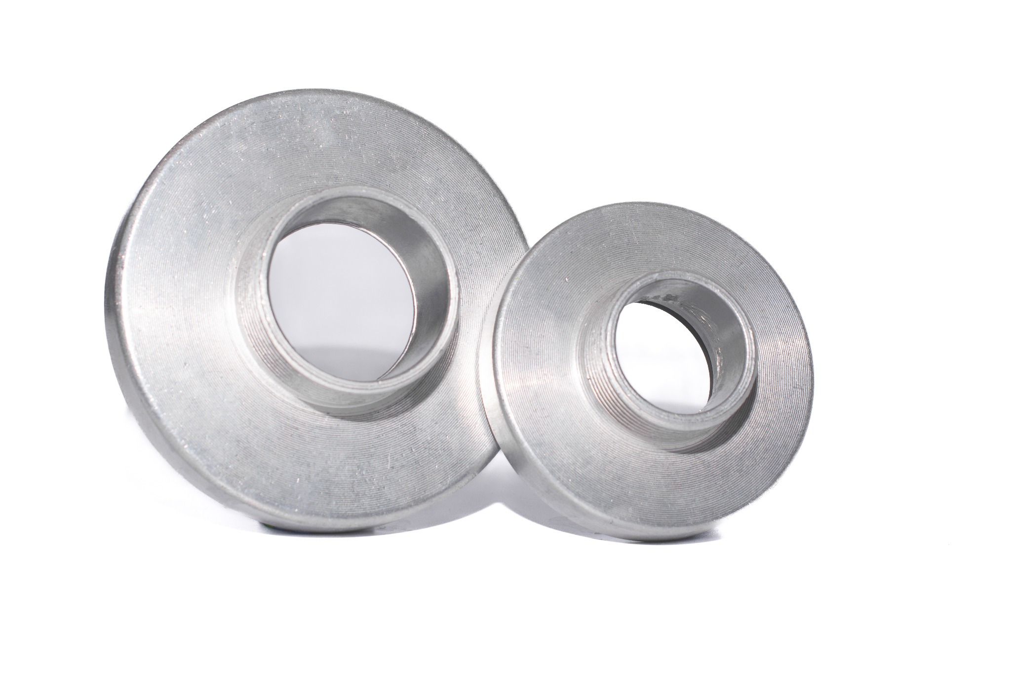 Dwie srebrne, okrągłe tuleje z gwintem wewnętrznym, różnej wielkości, leżące na białym tle. Widoczne ślady obróbki skrawaniem.