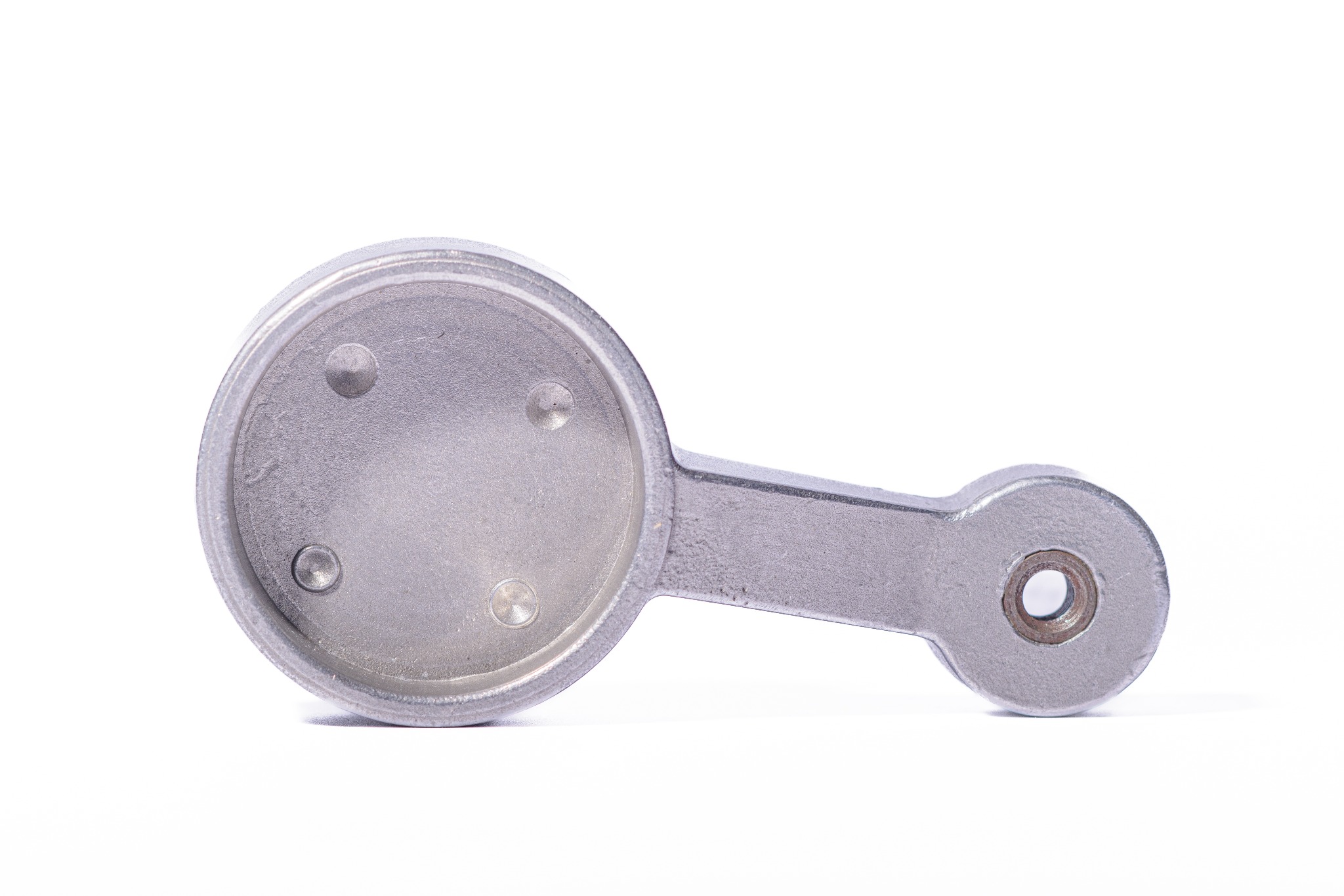 Metalowy element z okrągłą podstawą i uchwytem, widoczne ślady obróbki, szary odcień, na białym tle. Detal maszynowy.