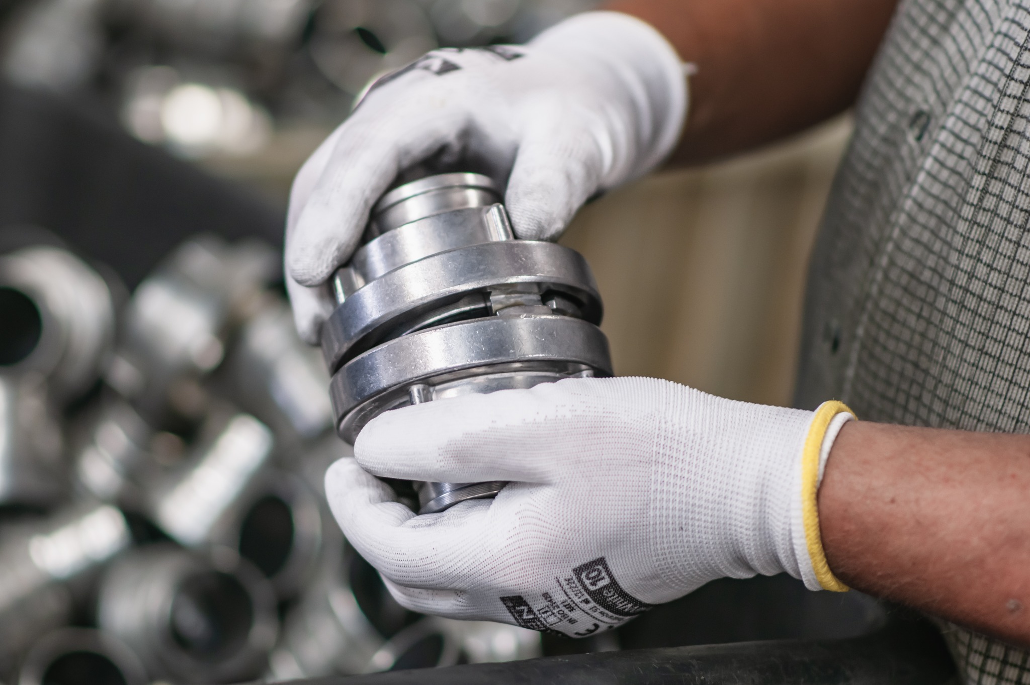 Ręce w białych rękawicach montują metalowy element z pierścieniami na tle innych metalowych części. Precyzyjna obróbka.