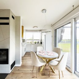 SOKOŁOWSKA architekt wnętrz - Jasne wnętrze z kominkiem i okrągłym stołem. Widok na kuchnię i taras. Parkiet na podłodze. Nowoczesny design z elementami złota.
