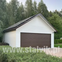 Biała hala z brązową bramą segmentową, otoczona zielenią. Na dachu widoczne panele solarne. Uwagę zwraca estetyczne wykończenie i wkomponowanie w otoczenie.